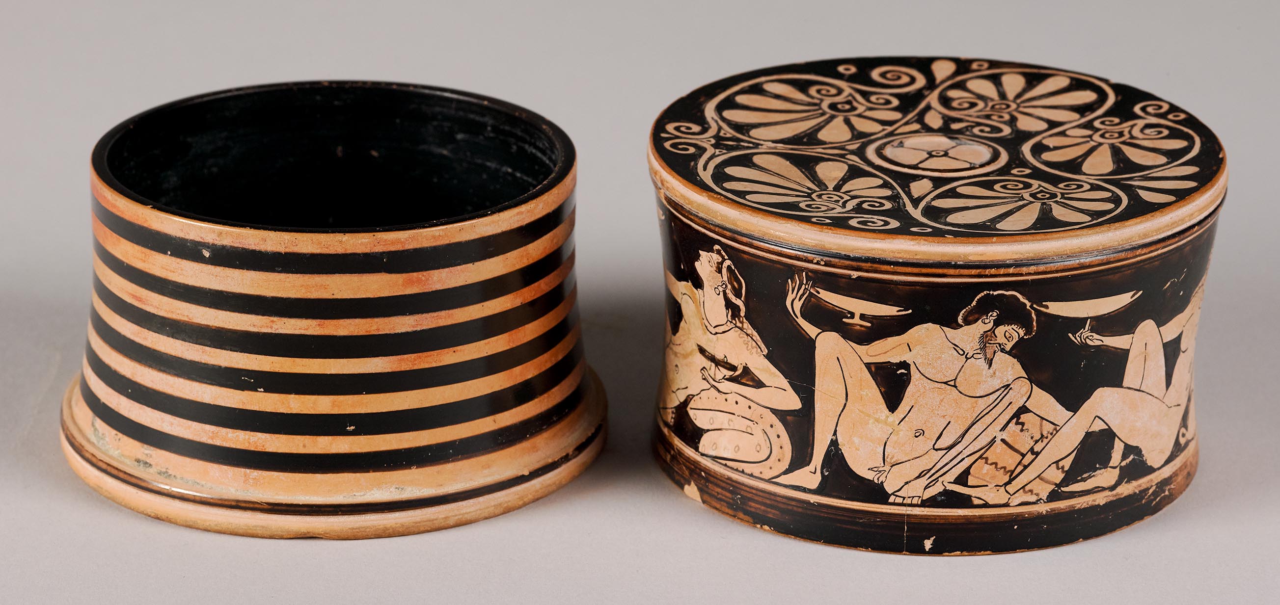 The striped body of the pyxis and the lid, the top with painted decoration and the lid depicting a symposion